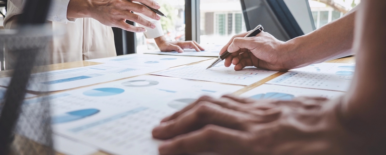 Photo closeup of two pairs of arms reviewing a printed presentation on an office desk