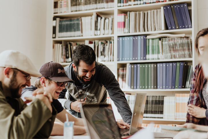Photo of 3 people huddled around a desk looking at a laptop